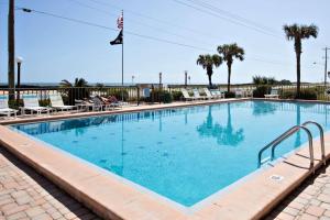 a large swimming pool with chairs and palm trees at Ocean Watch Condo Unit #105 in Ormond Beach