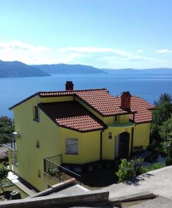 a yellow house with a red roof next to the water at Matea in Plomin