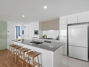 a kitchen with white appliances and wooden stools at Circle on Cavill - GCLR in Gold Coast