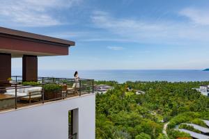 uma mulher de pé na varanda de um edifício com vista para o oceano em Grand Hyatt Sanya Haitang Bay Resort and Spa em Sanya