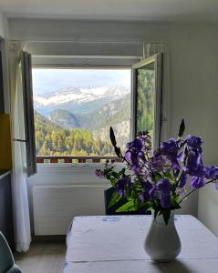 a vase of purple flowers on a table with a window at Hotel Zarera in Poschiavo