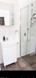 a white bathroom with a shower and a sink at Little Cottage Cessnock Hunter Valley in Cessnock