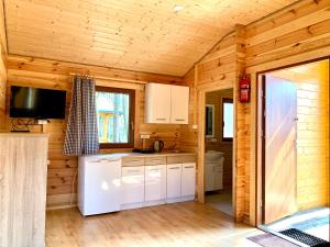 cocina con armarios blancos y TV en una cabaña de madera en Ośrodek Wypoczynkowy Jeziornik, en Borzechowo