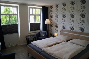 a bedroom with a bed and a chair and two windows at Hotel Villa Undine in Grömitz