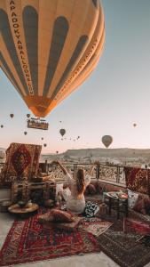 Kobieta siedząca na dywanie i oglądająca balony. w obiekcie Osmanli Cappadocia Hotel w Göreme