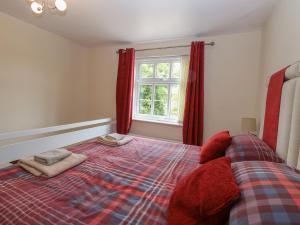 a bedroom with a bed with red curtains and a window at 2 Lock Cottages in Honing