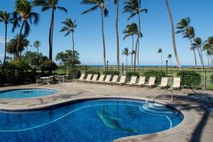 a swimming pool with chairs and palm trees at Kauhale Makai 335 in Kihei