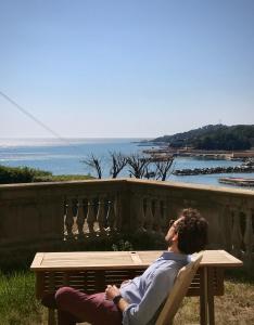 a man sitting on a bench looking out at the ocean at Appartamenti fronte mare in Castiglioncello