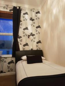 1 dormitorio con 1 cama con sábanas blancas y flores en la pared en Senlac Guesthouse, en Hastings