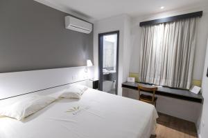 a bedroom with a large white bed and a desk at Uniclass Hotel Pinheiros in Sao Paulo