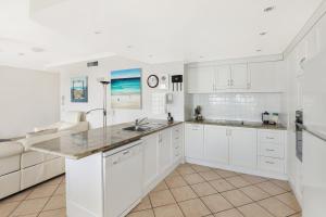 
a kitchen with white cabinets and white appliances at Coolum Seaside Apartments in Coolum Beach
