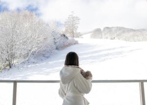 a woman holding a teddy bear looking out a window at snow at STARRY in Hakuba