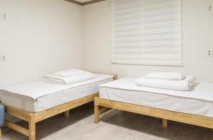 2 camas en una habitación con paredes blancas y ventana en Hwarang Guesthouse, en Gyeongju