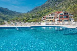 a swimming pool with chairs and mountains in the background at Lavender Bay Apartment B13 in Donji Morinj