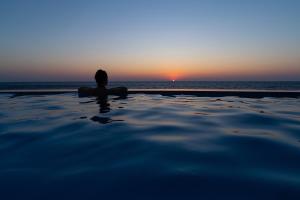 a person sitting in the water watching the sunset at Ikarian Endless Blue in Kouniádhoi