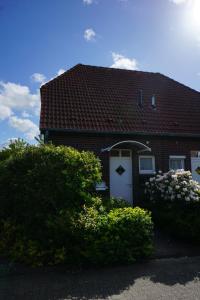a red brick house with a white door and some bushes at Günnis Perle am Harleufer in Carolinensiel