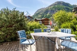 une table et des chaises sur une terrasse avec des montagnes en arrière-plan dans l'établissement Haus Alpine, à Zermatt
