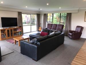 a living room with a black leather couch and a television at Waitomo Golf Ridge in Waitomo Caves