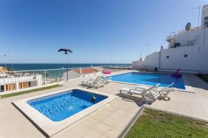 ein Swimmingpool mit Stühlen und das Meer im Hintergrund in der Unterkunft Apartamento sobre a praia in Olhos de Água