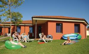 a group of people sitting in the grass in front of a house at Camping Bella Italia in Peschiera del Garda