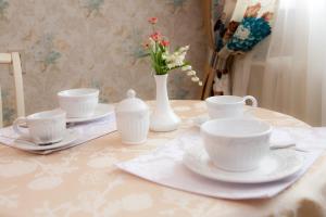 una mesa con tazas y platos blancos y un jarrón con flores en Vysotnik Hotel, en Chelyabinsk