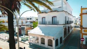 a white building with a blue roof next to a palm tree at Hotel Avenida Playa in Zahara de los Atunes
