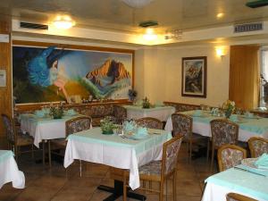アラッバにあるAlbergo Alpinoの白いテーブルと椅子が飾られた絵画のあるレストラン