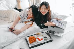 zwei Frauen, die mit einem Tablett Essen im Bett liegen in der Unterkunft Noursabah Boutique Bed Bangkok in Bangkok