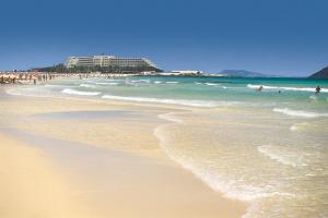 a beach with people swimming in the ocean and waves at Hotel Riu Palace Tres Islas in Corralejo