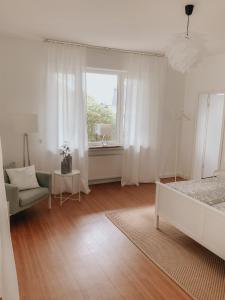a white bedroom with a bed and a chair and a window at Idyllische Stadtwohnung im Grünen in Siegen