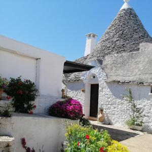 een wit huis met een rieten dak en bloemen bij Trulli la casa di Rosa in Alberobello
