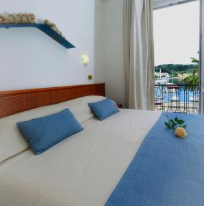 a bedroom with a white bed with blue pillows and a window at Hotel Della Baia in Portovenere