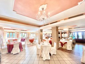 un restaurant avec des tables et des chaises blanches et un lustre dans l'établissement Hotel I Ginepri, à Quartucciu