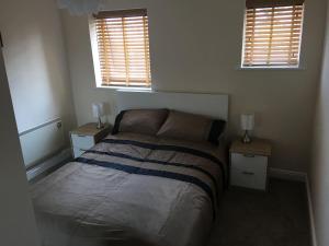 a bedroom with a bed with two night stands and two windows at Eaton Ford Green Apartment in Saint Neots