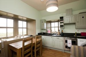 a kitchen with white cabinets and a wooden table and chairs at Balnakeil Beach Bothy in Durness