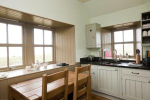 a kitchen with a wooden table and two windows at Balnakeil Beach Bothy in Durness