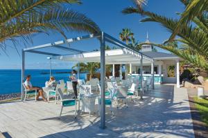 un restaurante en la playa con gente sentada en sillas en Hotel Riu Arecas - Adults Only, en Adeje