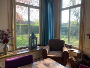 a living room with a chair and a table and windows at B&B Pastorie Jelsum in Jelsum