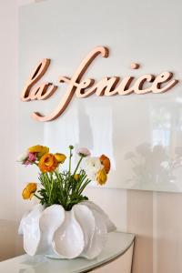 een witte vaas met bloemen op een tafel met een bord bij Hotel La Fenice in Rimini