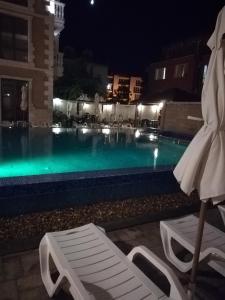 a swimming pool at night with a chair and an umbrella at Guest House Aristokrat in Obzor