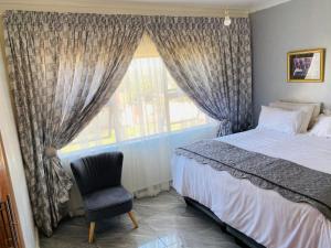 a bedroom with a bed and a chair and a window at River Valley Guest House in Butterworth
