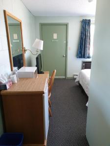 een kamer met een bureau, een bed en een spiegel bij Chimo Motel in Cochrane