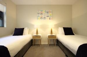 two twin beds in a room with two chairs at Kangaroo Bay Apartments in Hobart