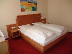 ein Schlafzimmer mit einem Bett mit weißer Bettwäsche und einem Gemälde in der Unterkunft Hotel Pension Futterknecht in Burgau