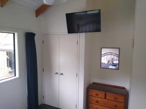 1 dormitorio con TV en la pared y vestidor en Kerigold Secluded Chalets Motel, en Kerikeri