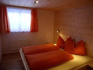 1 dormitorio con 1 cama con almohadas de color naranja y ventana en Dreimäderlhaus en Sankt Gallenkirch