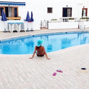 a woman in a blue hat sitting next to a swimming pool at Blue Island House on the hill in Los Cristianos