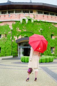 a woman walking with a red umbrella in front of a building at Citadel Inn Gastro Boutique Hotel in Lviv