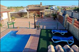 a swimming pool with two blue chairs in a yard at Chalet Puente de Tabla in Conil de la Frontera