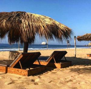 a straw umbrella and benches on a beach at Hotel Descalzo in Zipolite